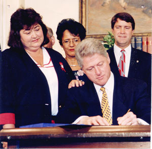Image of Bill Clinton signing the Ryan White Care Act while White's mother looks on.