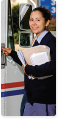 A female letter carrier with several pieces of mail is standing outside a USPS delivery truck, smiling and opening the door. She is dressed in a postal worker uniform with a navy sweater.
