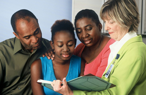 A teenager, her parents and a female doctor standing together. They are looking at information in a book.