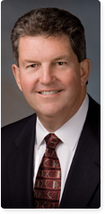 A portrait style image of Patrick Donahoe, the current Postmaster General.  He is wearing a suit and a patterned red tie.