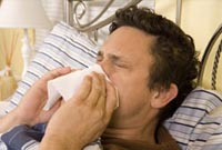Sick man in bed blowing his nose.