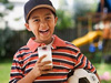 Young boy in backyard with a glass of milk in his hand and a soccer ball under his arm.