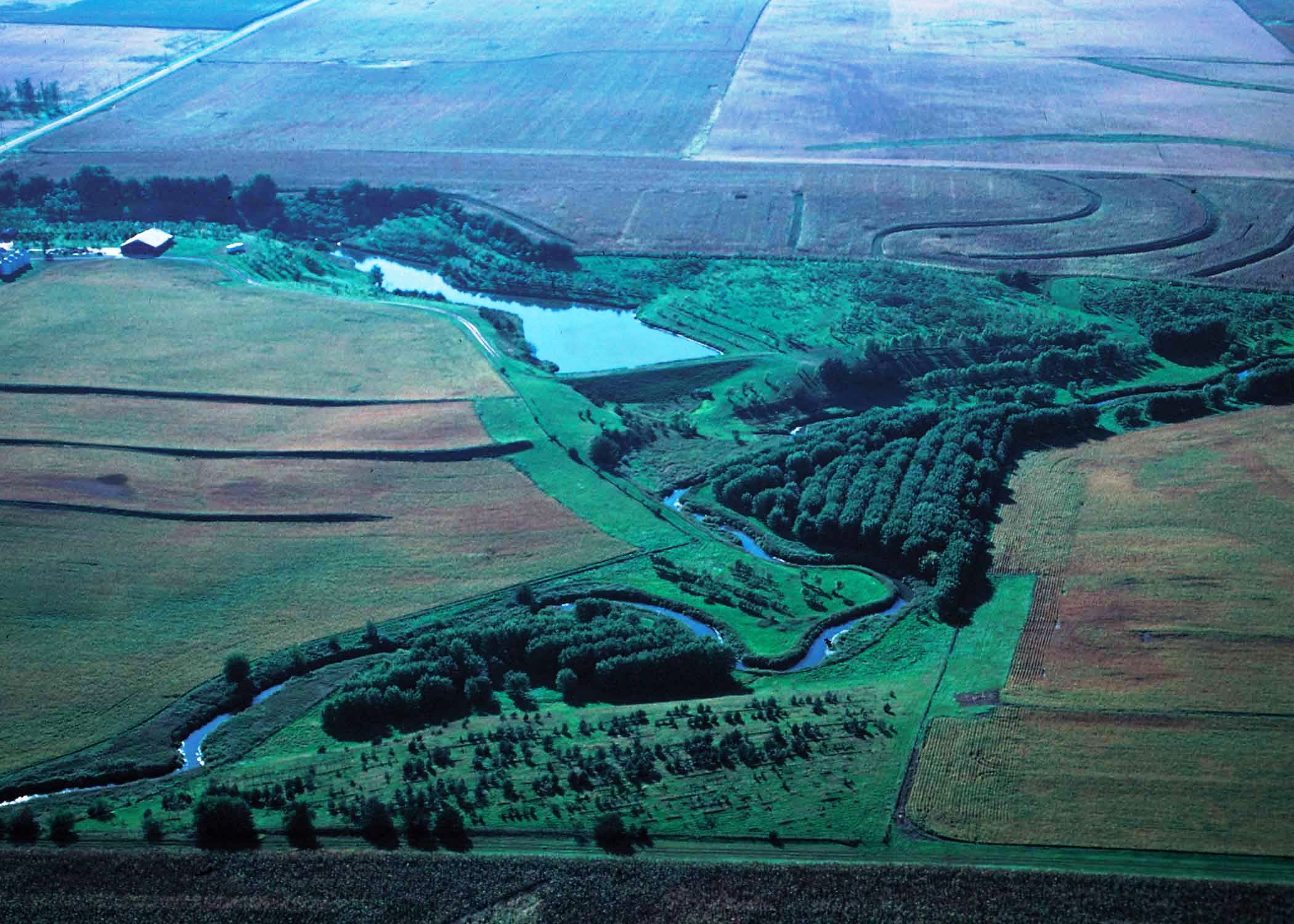 Oblique aerial view of a small watershed flood prevention structiure with green fields.