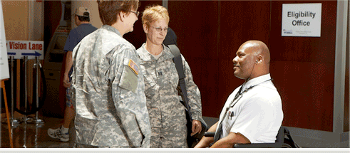 Two service women speaking to a man in a wheelchair.