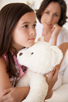 Mother on the phone looking at her daughter who is holding a teddy bear