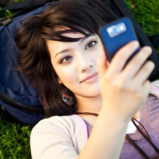 Una niña recostada en el césped mirando un teléfono celular