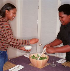 A girl and a boy scooping a salad into bowls.