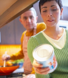 Woman reading nutrition label on canned good with man looking over her shoulder.  