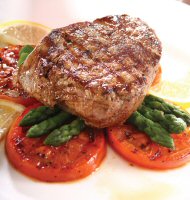 A cooked steak presented atop asparagus and tomatoes