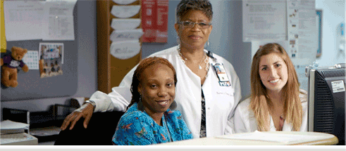 Three smiling nurses seated at a nurses station.