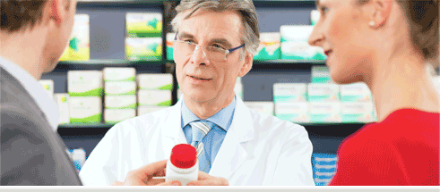 A pharmacist handing a pill bottle to a man as a woman looks on.