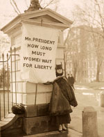 Woman standing near the White House holding a suffrage banner.