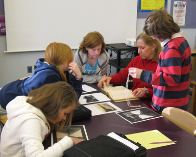 photo of a teacher and students around a table, looking at documents and photographs