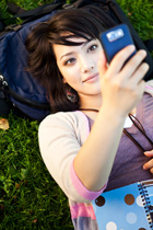 Girl laying on the grass looking up at a cell phone