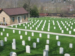 A photo of two levels of upright headstones aligned vertically on the lawn with a cement sidewalk dividing the grounds in two areas.