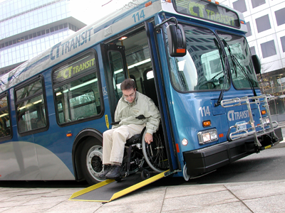 Rider manuevering wheelchair off of low-floor bus using ramp.