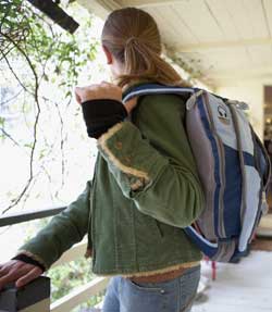 Photograph of a young person leaving a house and carrying a backpack.