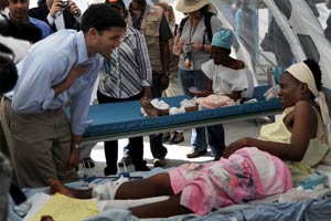 USAID Administrator Rajiv Shah leans in to speak to a Haitian woman on an a hospital bed