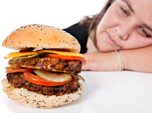 Photo of an overweight young woman resting her head on her arm and gazing longingly at a forbidden cheeseburger.