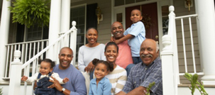 A large, smiling family sits together on their front porch