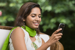 Photograph of a young woman sitting outdoors and looking at her smart phone.