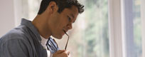 young male studying with glasses held to mouth