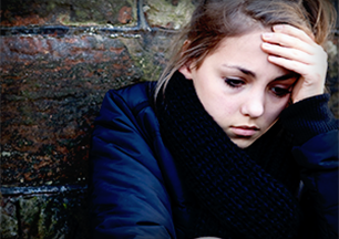  a teen girl, sitting against a brick wall thinking