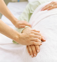 A caregiver is holding the hand of their loved one who is resting in bed