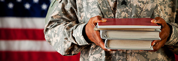 Service member holding books, with the American flag in the background