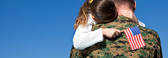 Girl holding flag hugging father in uniform.