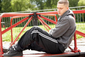 Photograph of a young man sitting in a playground looking sad.