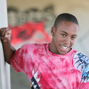 Photograph of an African American young man smiling and leaning on a wall
