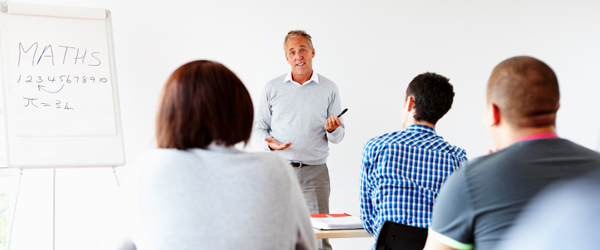 A man standing at a white board teaching a small class of adult students