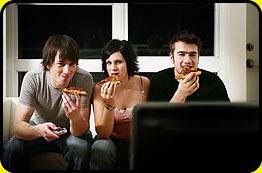 Image of a group of teens watching television and eating pizza 