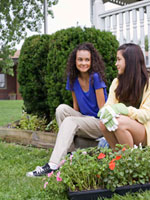 Two girls bonding next to a flower bed.