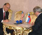 Dr Roger I Glass signs agreement on table, Russian representative across table signs, US and Russian flags on table