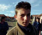 Young Bulgarian man looks into camera, village buildings and other people in background