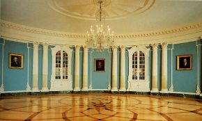 The Treaty Room at the State Department with curving blue walls,  inlaid wooden floor, white columns, book cabinets, portraits and chandelier. 