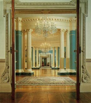 The elliptical form of the Treaty Room at the State Department, is at the center of the suite and features curving blue walls, inlaid wooden floor, white columns, and chandeliers. 