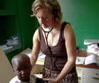 Dr Manning in an exam room with stethoscope in ears holds it to a young boy’s back, she looks down at him, he looks at camera