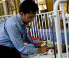 Male doctor sits on edge of crib with lowered rail, uses stethoscope to examine baby