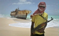 Date: 09/23/2012 Description: In this Sunday, Sept. 23, 2012 file photo, masked Somali pirate Hassan stands near a Taiwanese fishing vessel that washed up on shore after the pirates were paid a ransom and released the crew, in the once-bustling pirate den of Hobyo, Somalia. © AP Image