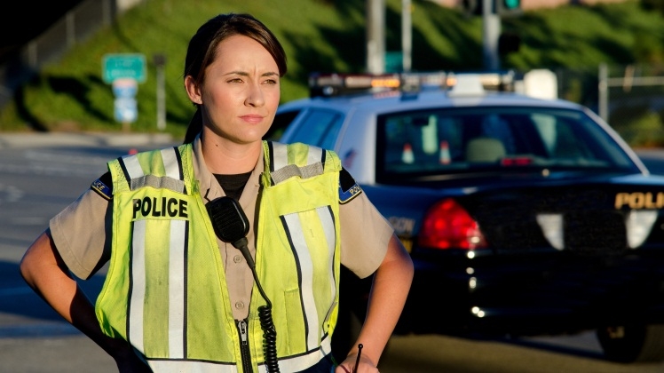 Photo of a woman police officer looking serious while standing be her squad car