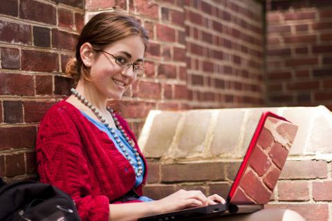 Girl smiling, using laptop against brick wall