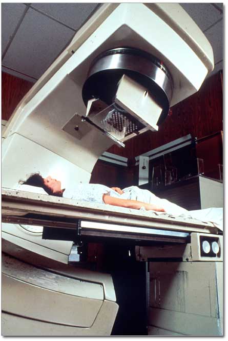 A white adult female patient being readied for radiation therapy. She is lying on a table, covered with a white cloth.