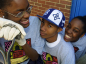 Photograph of three young people smiling and holding gardening tools.
