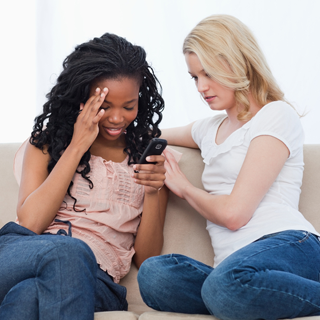 Two women sitting on a couch.  Upset woman is being comforted by the other woman.