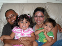 A smiling man and woman sitting on a couch hold two children in their laps