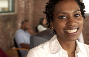 Photograph of a young African American woman with young people training at computers behind her.