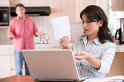 Mujer sentada frente a su computadora portátil habla sobre dinero con su esposo.